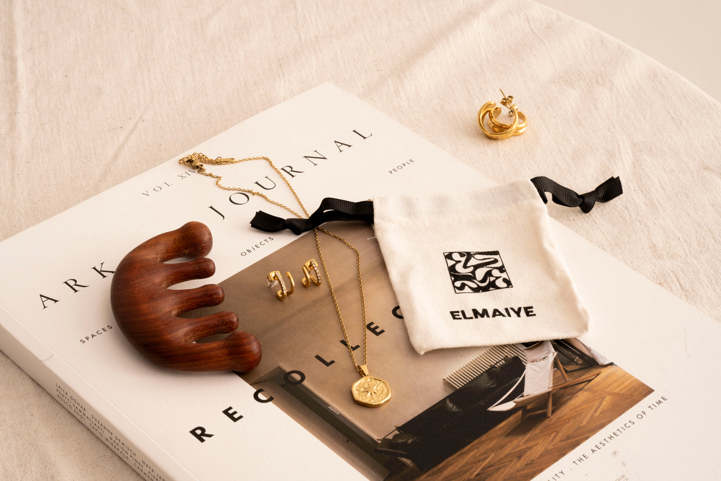 Elmaiye jewellery and a book on a light surface with 'ELMAIYE' branding.