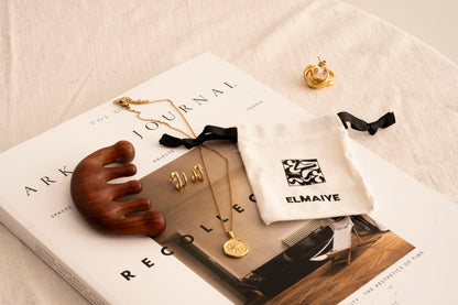 Elmaiye jewellery and a book on a light surface with 'ELMAIYE' branding.